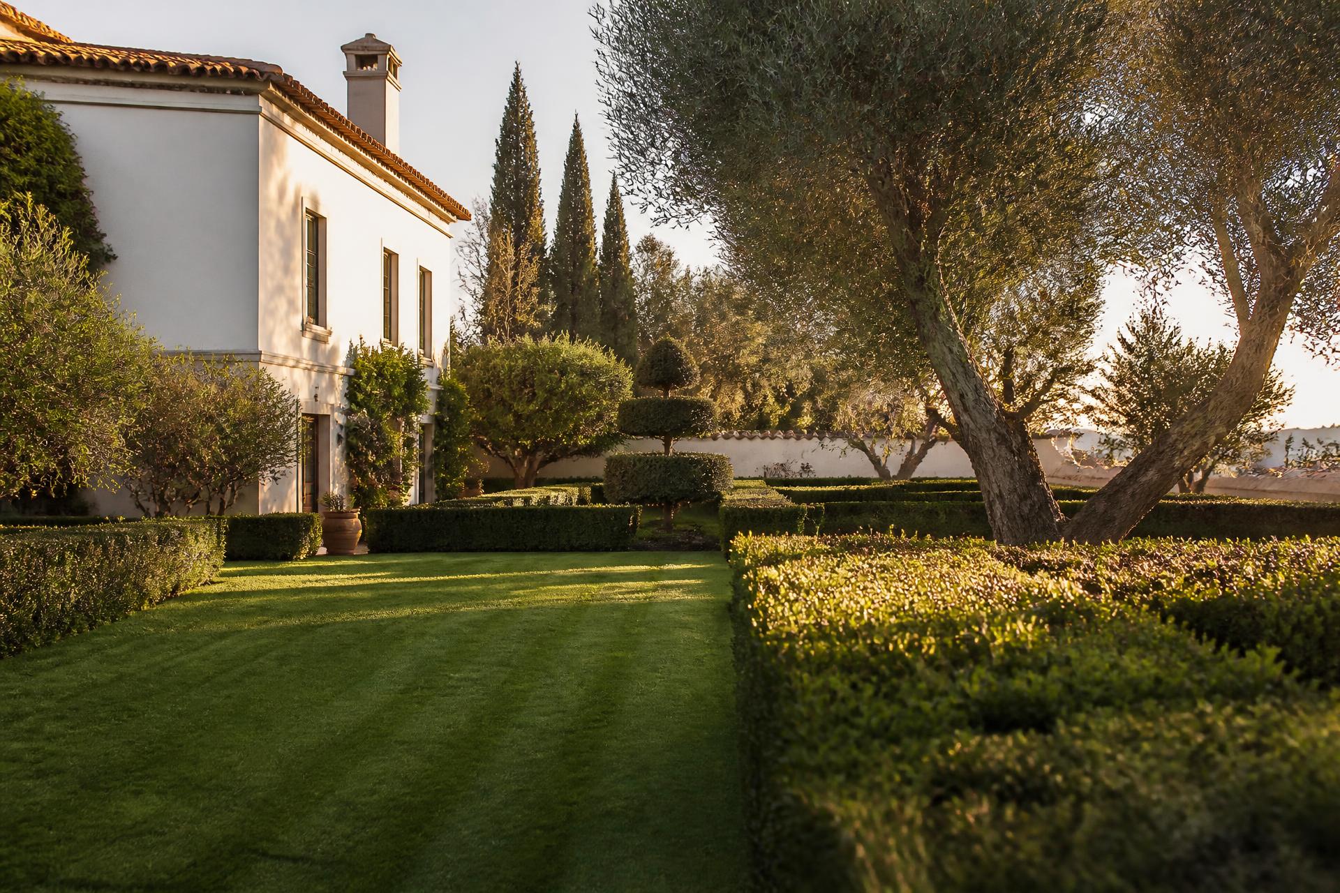 Jardim privado tratado, com relvado riscado e sebes aparadas, ao fim da tarde